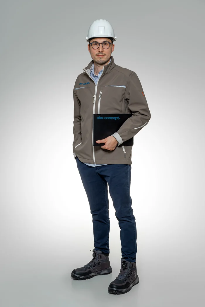 Sebastian Adam von cbs-concept in Arbeitsjacke mit weißem Schutzhelm und Projektmappe unter dem Arm