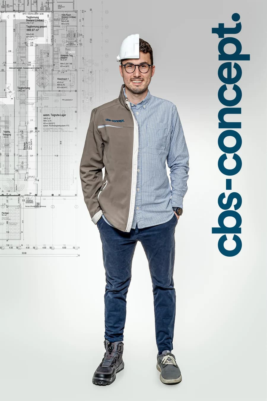 Sebastian Adam of cbs-concept, half in work jacket with hard hat, half in a shirt, in front of the layout plan of a bakery production